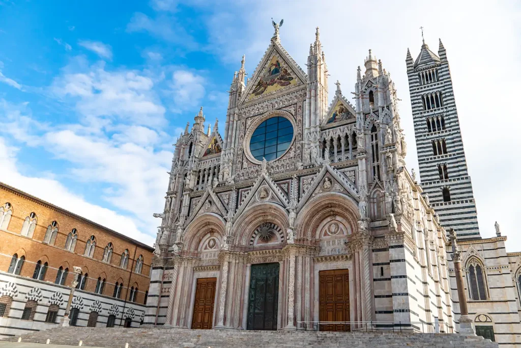 Façade gothique de la cathédrale de Sienne en Toscane, avec ses sculptures, sa grande rosace et son campanile rayé de marbre blanc et noir