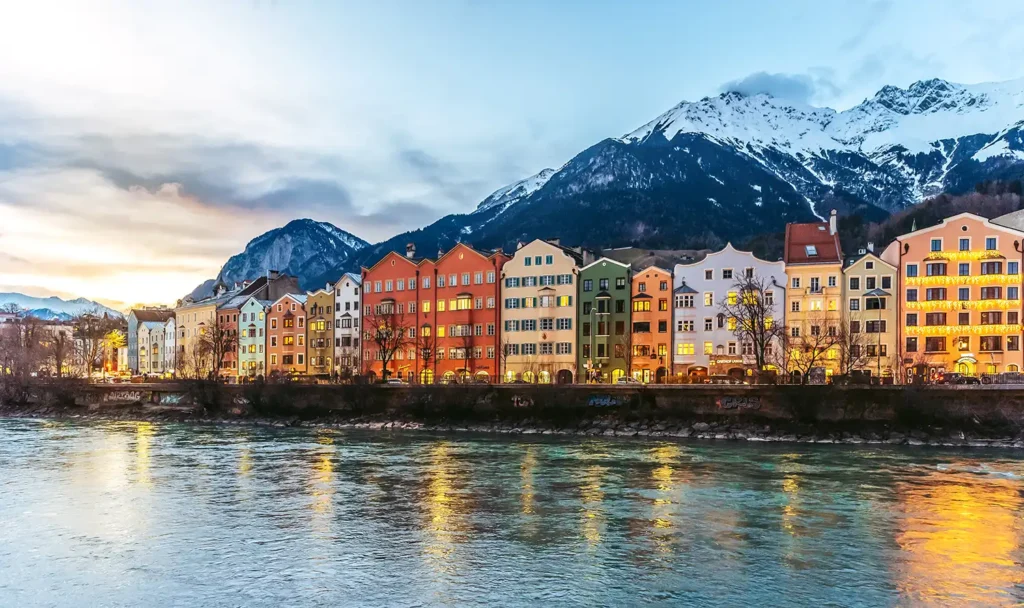 Façades colorées du quartier de Mariahilf à Innsbruck, reflétées dans la rivière Inn, avec les montagnes enneigées du Tyrol en arrière-plan