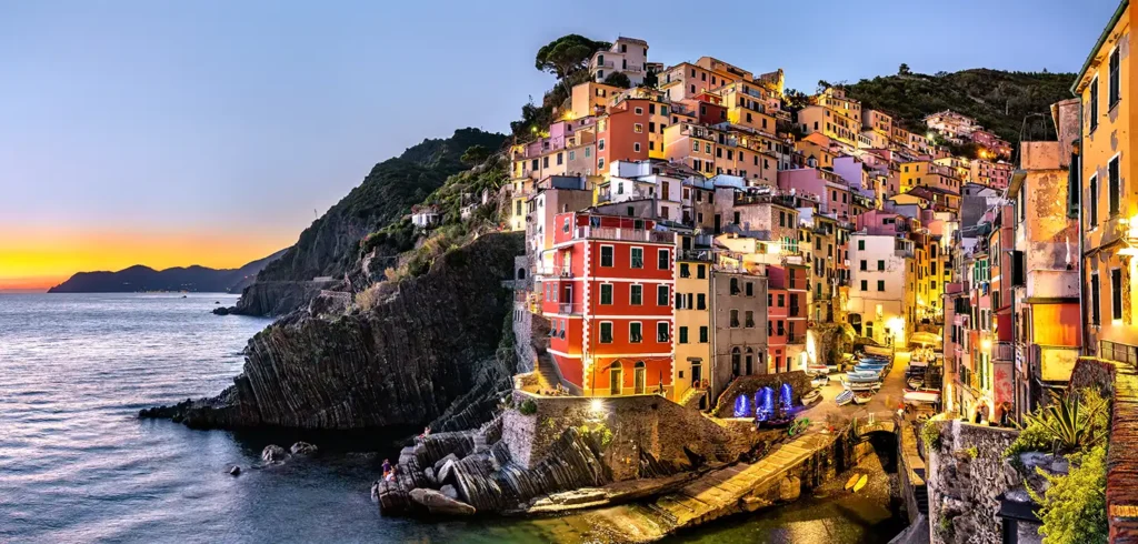 Maisons colorées d’un village des Cinque Terre en Ligurie, construites à flanc de falaise au-dessus d’un petit port méditerranéen au coucher du soleil